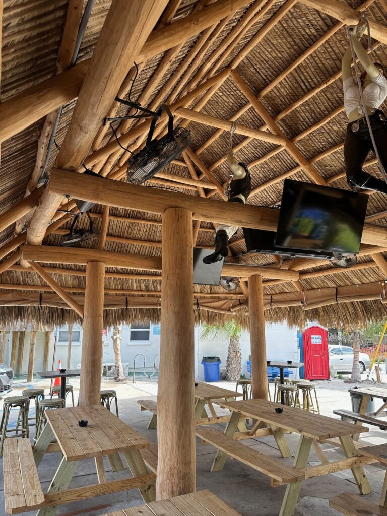 Under Ka'Tiki's thatched roof: wooden picnic tables, bar stools, TV and ceiling fans